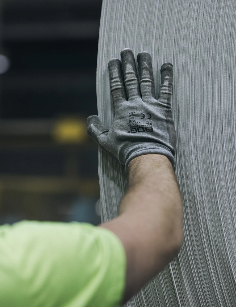 Ein Arbeiter mit Schutzhelm und Handschuhen prüft eine Metallrolle in der Produktion